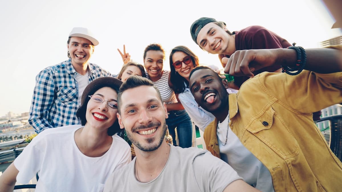 A diverse group of young friends laughing together in a group selfie outdoors.
